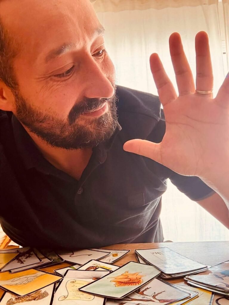 Greg, la main levée, devant un tirage de cartes
