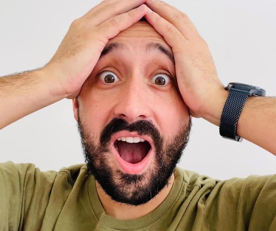 Greg, surpris et ravi, les mains sur la tête